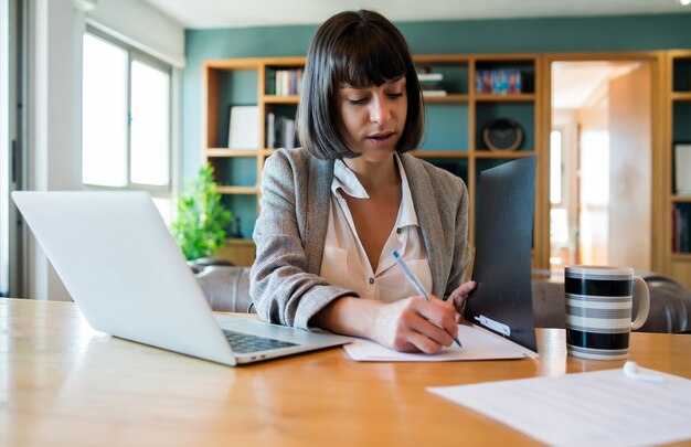 Portrait de jeune femme travaillant à domicile avec ordinateur portable et fichiers. Concept de bureau à domicile. Nouveau style de vie normal.