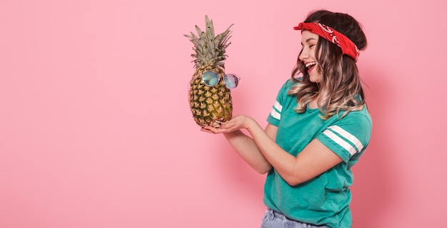 Portrait d'une jeune fille à l'ananas sur un mur rose