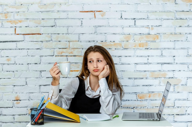 Photo gratuite portrait de jeune fille assise derrière son bureau et regardant sa tasse