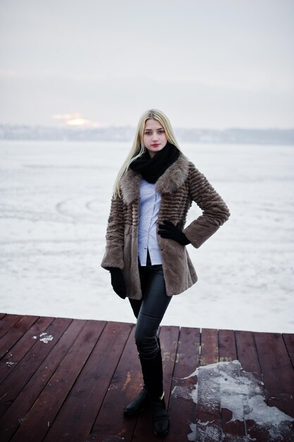 Portrait de jeune fille blonde élégance dans un manteau de fourrure au fond de la jetée rivière brumeuse sur la glace d'hiver