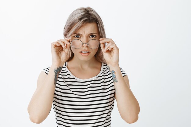 Portrait de jeune fille blonde inquiète avec des lunettes posant en studio