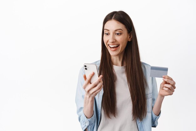 Portrait de jeune fille brune a l'air excité à l'écran du smatphone lisant l'offre proo de paiement en ligne sans contact et de commande par téléphone avec carte de crédit Espace de copie