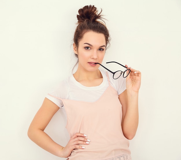 Portrait de jeune fille brune belle modèle de fille avec du maquillage nude dans des vêtements de hipster rose d'été coloré posant près du mur. lunettes mordantes