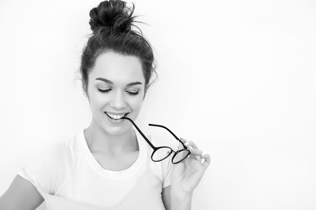 Portrait de jeune fille brune belle modèle de fille avec du maquillage nude dans des vêtements de hipster rose d'été coloré posant près du mur. lunettes mordantes