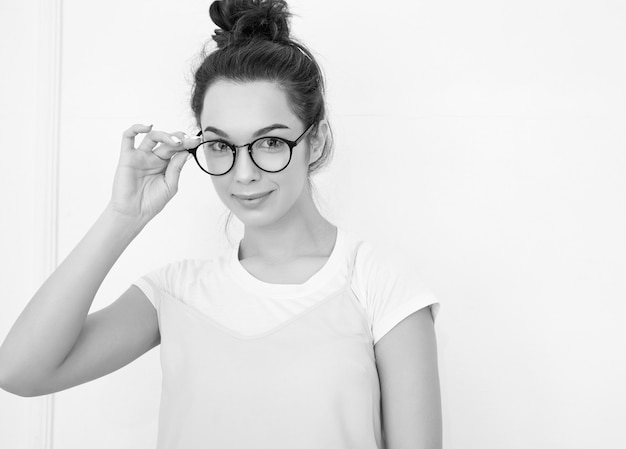 Portrait de jeune fille brune belle modèle de fille avec du maquillage nude dans des vêtements de hipster rose d'été coloré posant près du mur. regardant joyeusement