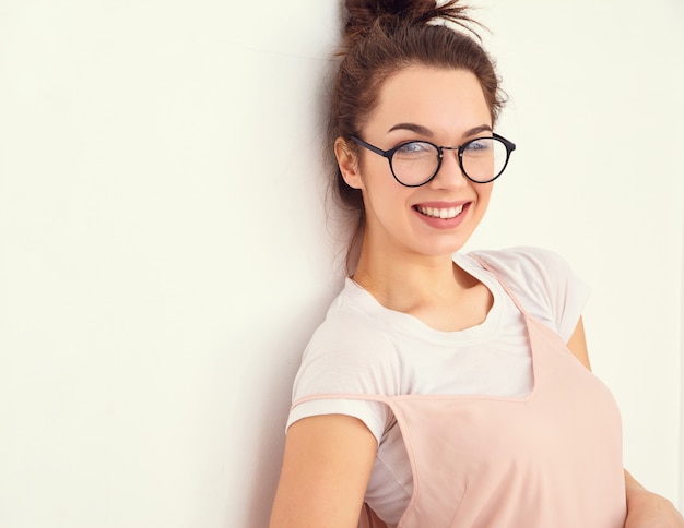 Portrait de jeune fille brune belle modèle de fille avec du maquillage nude dans des vêtements de hipster rose d'été coloré posant près du mur. regardant joyeusement