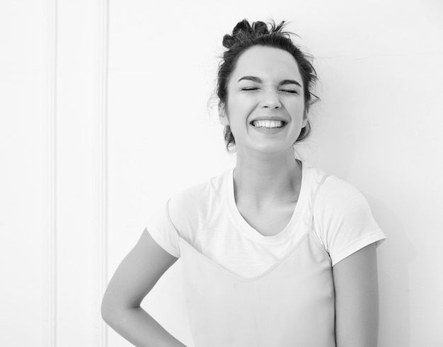 Portrait de jeune fille brune belle modèle de fille avec du maquillage nude dans des vêtements de hipster rose d'été coloré posant près du mur. regardant joyeusement