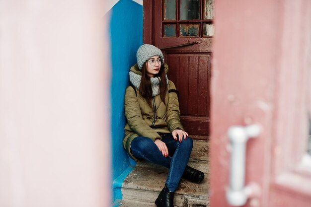 Portrait de jeune fille brune en écharpe grise et lunettes de chapeau contre l'entrée