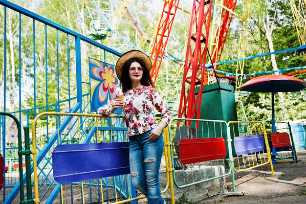 Portrait de jeune fille brune à lunettes roses et chapeau avec de la glace au parc d'attractions