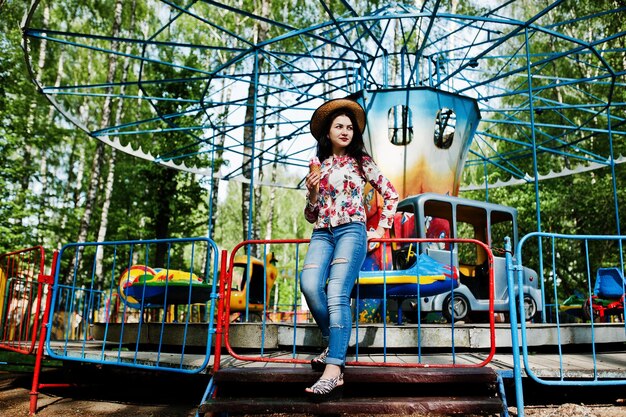 Portrait de jeune fille brune à lunettes roses et chapeau avec de la glace au parc d'attractions