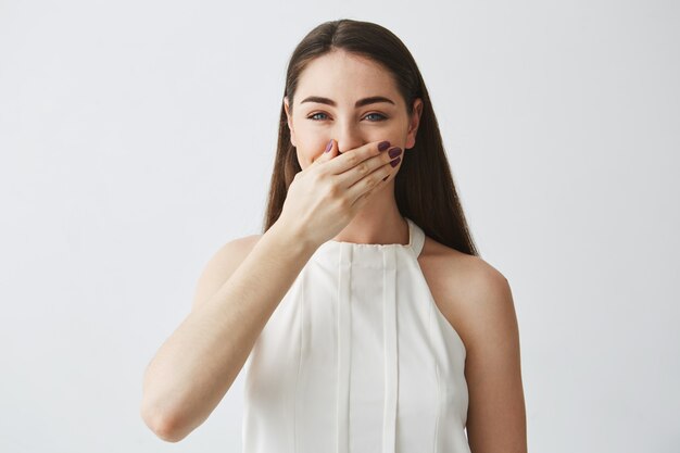 Portrait de jeune fille brune en riant couvrant la bouche avec la main.