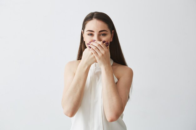 Portrait de jeune fille brune en riant couvrant la bouche avec la main.