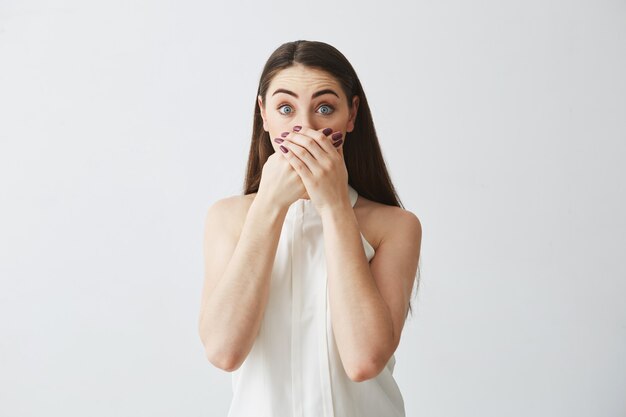 Portrait de jeune fille brune surprise couvrant la bouche avec la main.