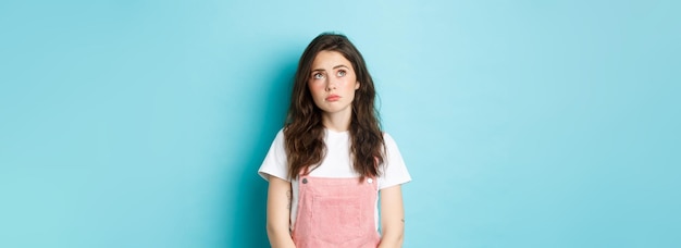 Photo gratuite portrait d'une jeune fille brune triste et sombre avec un maquillage glamour regardant le coin supérieur gauche bouleversé et pensif se sentant de mauvaise humeur debout sur fond bleu