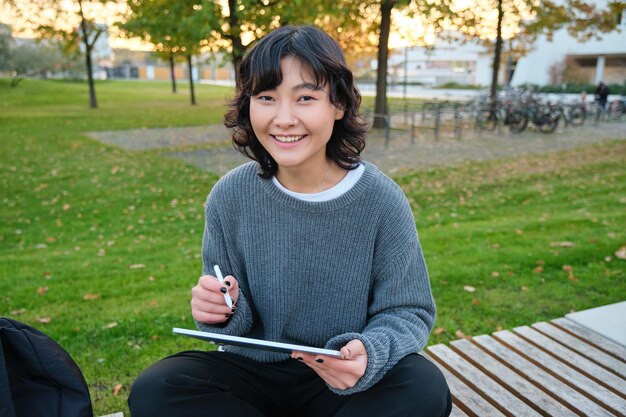 Portrait d'une jeune fille coréenne souriante graphiste dessinant sur une tablette numérique avec un stylo t