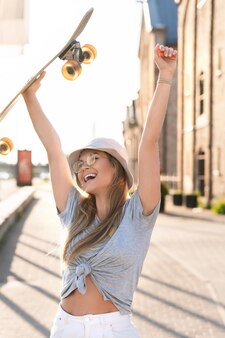 Portrait de jeune fille élégante portant un chapeau de panama avec un longboard dans une ville