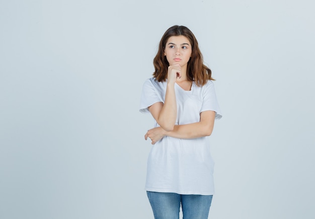 Portrait de jeune fille étayant le menton sur place en t-shirt blanc et à la vue de face pensive