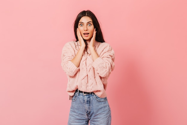 Portrait de jeune fille étonnée en jeans et pull rose. Dame en état de choc regardant la caméra.