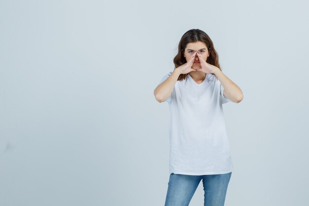 Portrait de jeune fille gardant les mains pour dire secret en t-shirt blanc, jeans et à la vue de face sérieuse