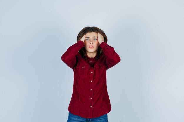 Portrait de jeune fille gardant les mains sur la tête en chemise décontractée et à l'air agité