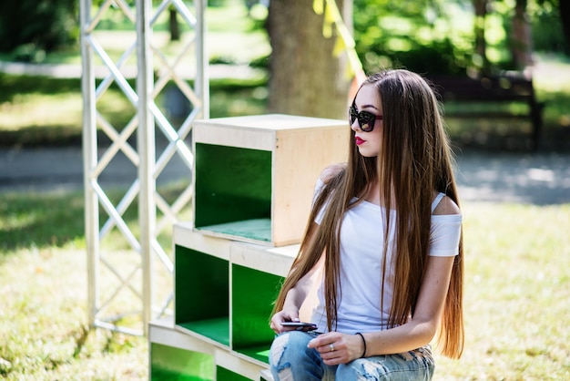 Portrait d'une jeune fille habillée à la mode posant sur des caisses en bois dans le parc par une journée ensoleillée