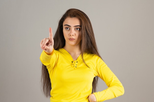 Portrait de jeune fille en haut jaune regardant et regardant sur un mur gris.