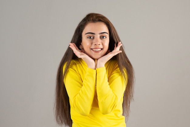 Portrait de jeune fille en haut jaune regardant et souriant sur un mur gris.