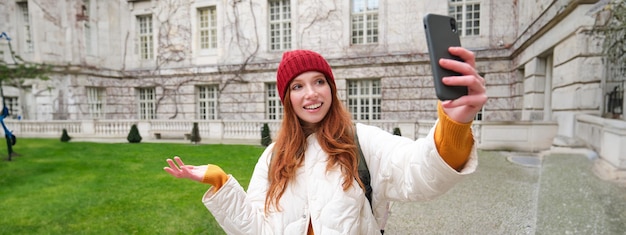 Photo gratuite portrait d'une jeune fille heureuse posant près des conversations vidéo des attractions de la ville et démontre un point de repère