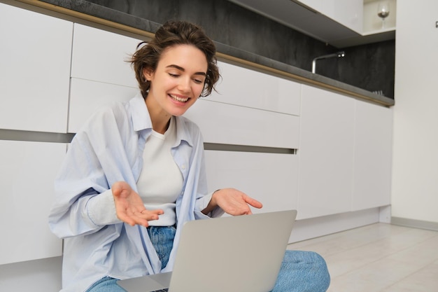 Portrait d'une jeune fille indépendante qui se connecte à des réunions en ligne, à des discussions vidéo sur un ordinateur portable, assise sur une table de cuisine.