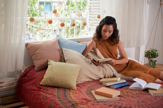 Portrait de jeune fille lisant des livres de texte dans son lit