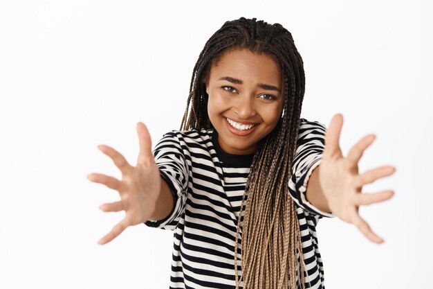 Portrait d'une jeune fille noire souriante tendant les mains pour recevoir prendre qch dans ses bras étreignant debout sur fond blanc