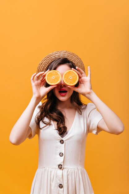 Portrait de jeune fille en robe blanche et chapeau couvrant les yeux avec des moitiés orange.