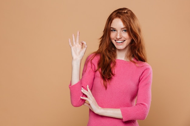 Portrait d'une jeune fille rousse souriante à la recherche de faire le geste OK