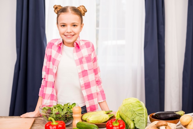 Portrait d&#39;une jeune fille souriante, debout derrière la table avec des légumes frais