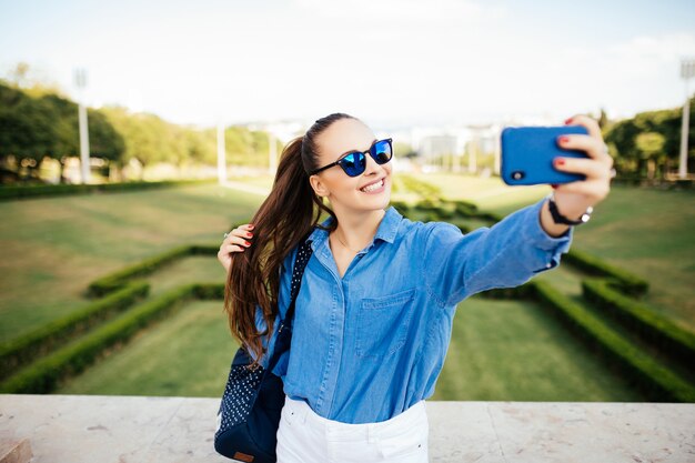 Portrait d'une jeune fille souriante à lunettes de soleil faisant photo selfie dans le parc