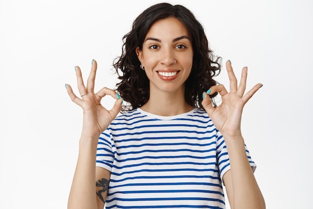 Portrait d'une jeune fille souriante montre des signes d'accord d'accord semblent satisfaits recommandent une bonne entreprise qualité parfaite louange bon travail bien fait debout heureux sur fond blanc