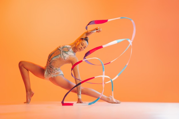 Portrait de jeune fille sportive formation d'artiste de gymnastique rythmique isolé sur fond de studio orange en néon lght