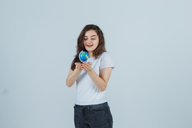 Portrait de jeune fille tenant un globe en t-shirt, jeans et à la vue de face étonné