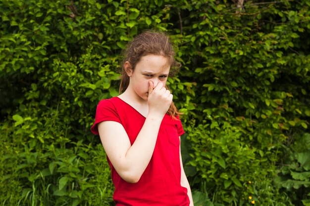 Portrait de jeune fille tenant le nez dans la nature verdoyante, regardant la caméra