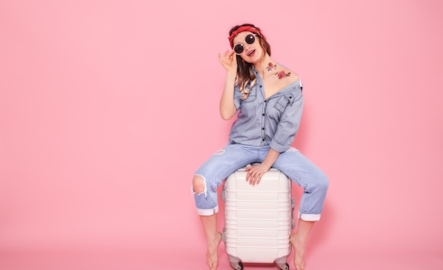 Portrait d'une jeune fille avec une valise sur fond rose