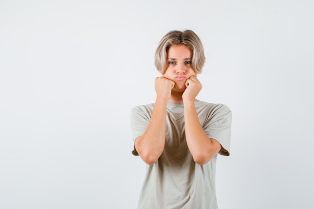 Portrait de jeune garçon adolescent boudant avec des joues gonflées s'appuyant sur les mains en t-shirt et à la vue de face déçu