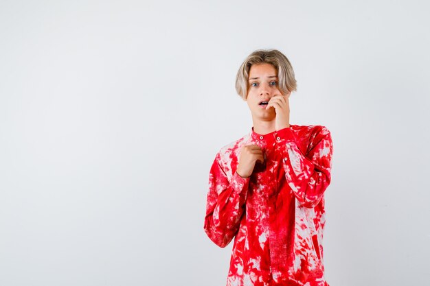 Portrait de jeune garçon adolescent gardant la main sur la joue en chemise et à la vue de face effrayée