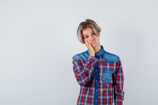 Portrait de jeune garçon adolescent avec la main sur la joue en chemise à carreaux et à la vue de face déçu