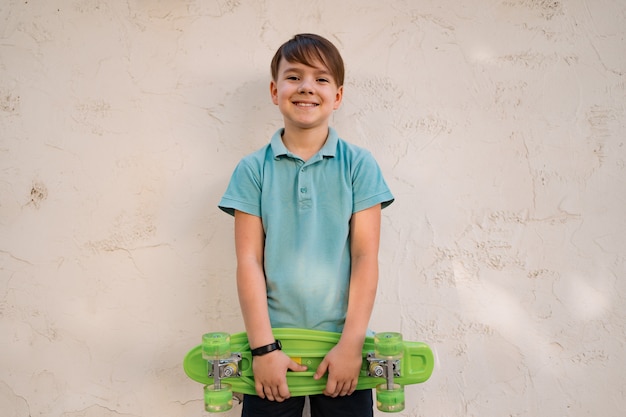 Portrait Jeune garçon souriant cool en polo bleu posant avec PENNY BOARD dans les mains