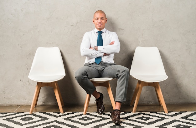 Portrait d&#39;un jeune homme d&#39;affaires souriant assis sur une chaise avec les bras croisés