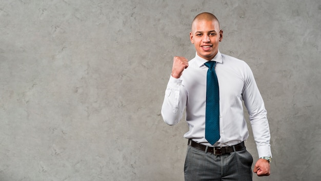 Portrait d&#39;un jeune homme d&#39;affaires souriant, debout contre le mur gris, serrant son poing