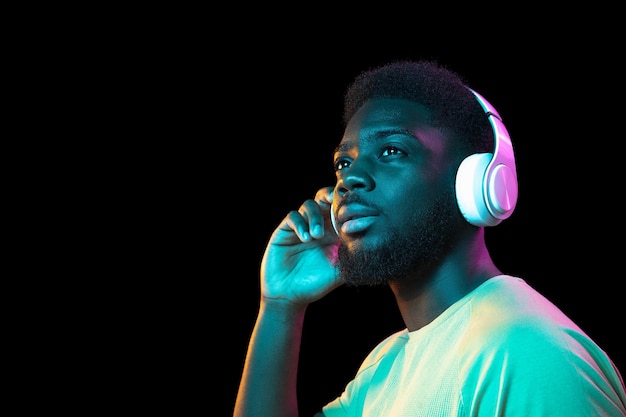 Portrait de jeune homme africain sur fond de studio sombre en néon Concept d'émotions humaines expression faciale annonce de vente pour les jeunes