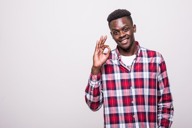 Portrait d'un jeune homme africain heureux en chemise blanche montrant le geste ok isolé