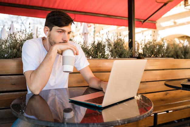 Portrait de jeune homme à l'aide de son ordinateur portable alors qu'il était assis dans un café. Concept de technologie et de style de vie.