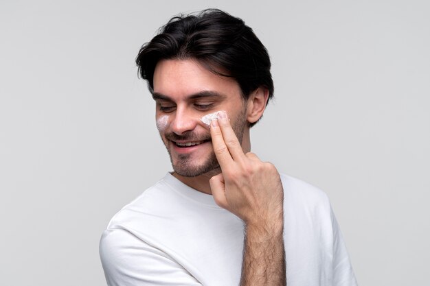 Portrait d'un jeune homme appliquant une crème hydratante sur son visage